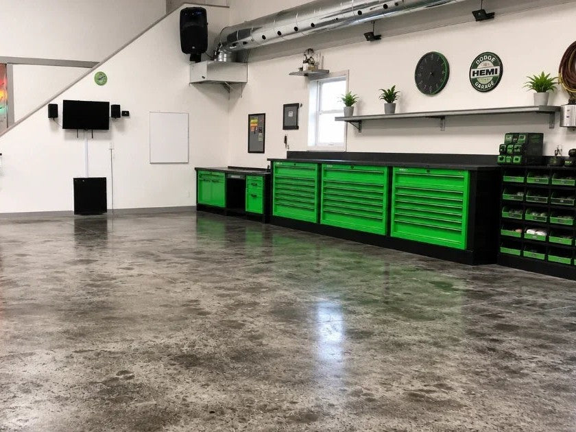 A shop floor finished in black, its mottled dark gray surface reflecting the green tool chests along the wall