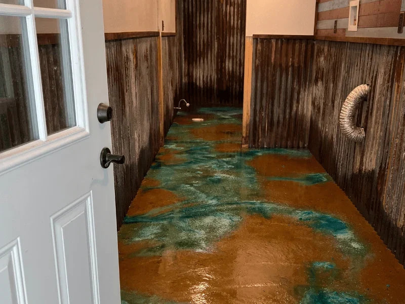 An eclectic bathroom with a vibrant, acid-stained concrete floor in hues of azure blue and earthy tones, blending a rustic wooden wall finish with a splash of modern color