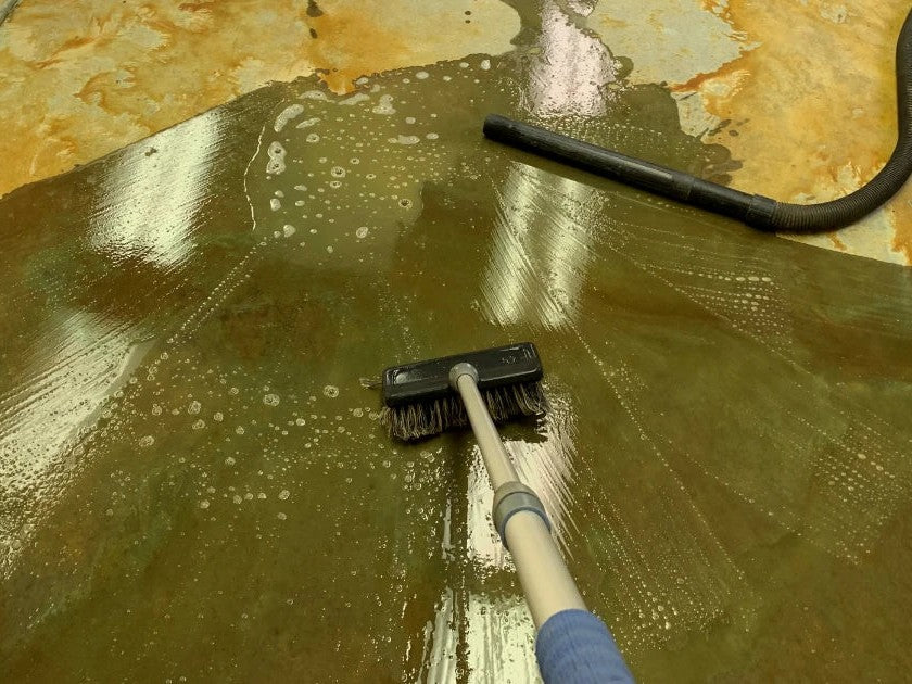 Scrubbing an acid-stained concrete floor with a deck brush and wet/dry vacuum to lift residue before sealing