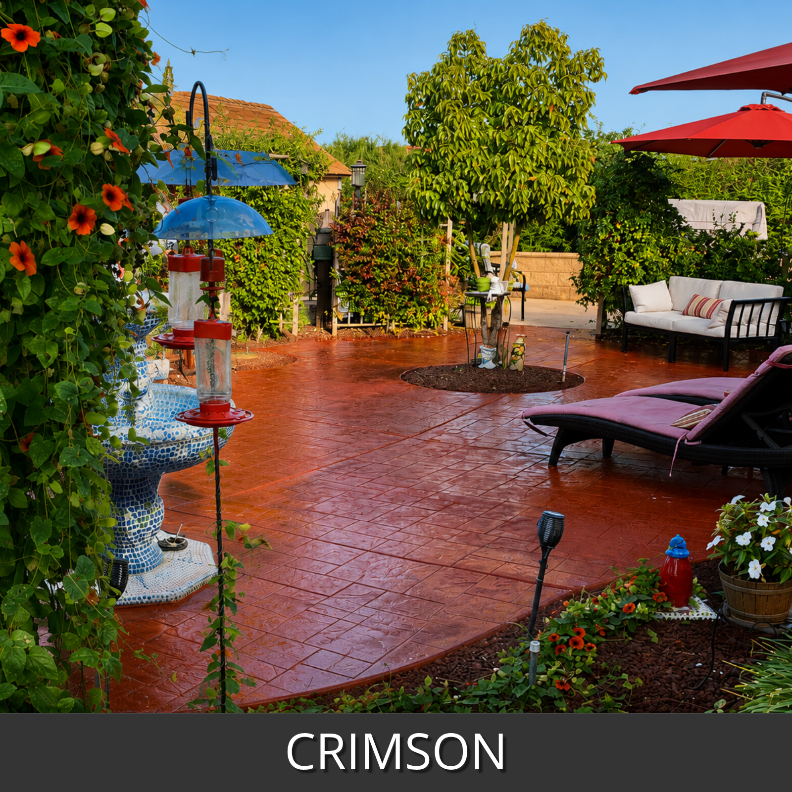 A landscaped outdoor patio with a crimson stained stamped concrete floor greenery, flowers, lounge chairs, umbrellas, and a bench in the background.