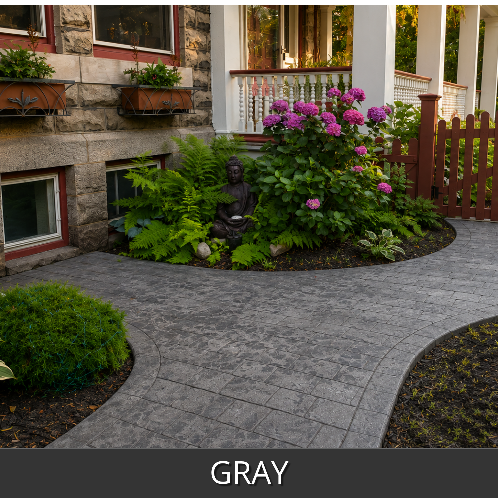 Gray refinished stamped concrete pavers installed in a landscaped garden bed beside a stone house, with green plants, pink flowers, a small statue, and a wooden fence