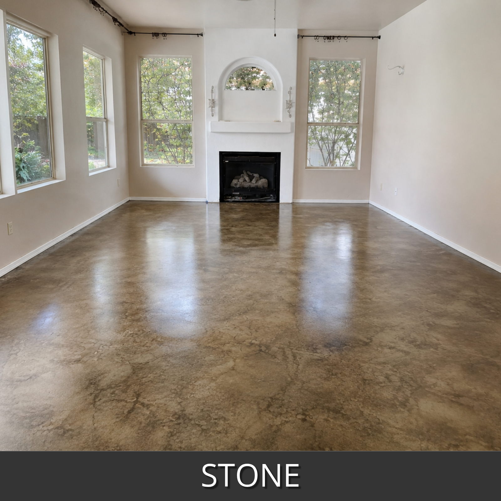 A large empty room with a polished stone colorwave water based stained floor in warm brown and beige tones, white walls, tall windows, and a fireplace