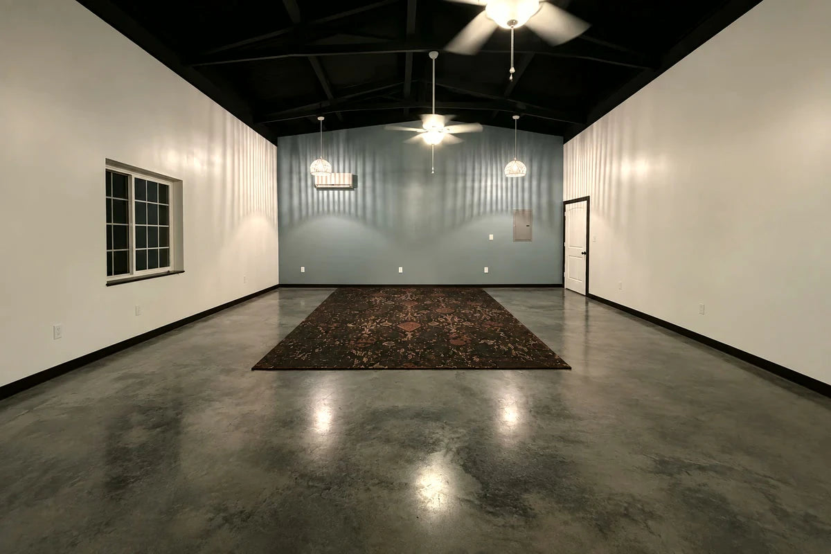 Tinted concrete floor in a large room with a dark rug, AcquaTint™ in 506 Charcoal finished with ProWax Polish™ Gloss