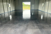 Tinted concrete floor in a metal barndominium shop with the roll-up door open, AcquaTint™ in 506 Charcoal finished with ProWax Polish™ Satin