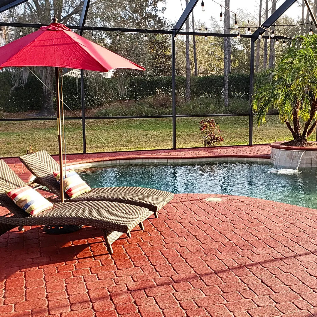 Pool area with lounge chairs and a red umbrella on a brick patio.
