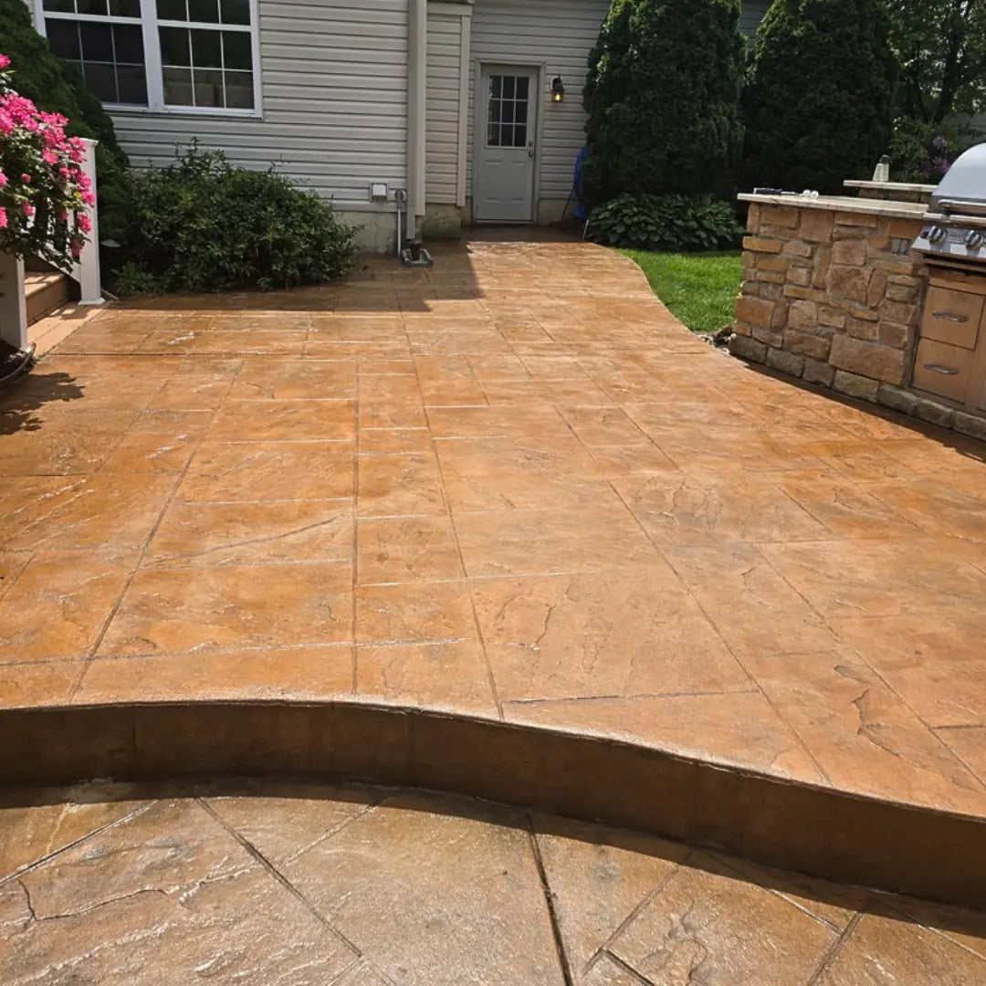 Stained concrete patio in a backyard with a house and outdoor furniture in the background.