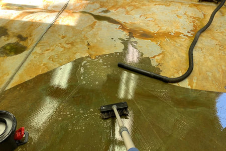 Scrubbing ProClean Neutralizer into an acid-stained concrete floor with a nylon brush while a wet/dry vacuum removes the rinse water