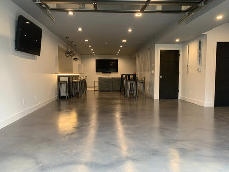 A basement with protective coverings on the lower walls and bar, showing the floor after the application of the first coat of AcquaTint stain