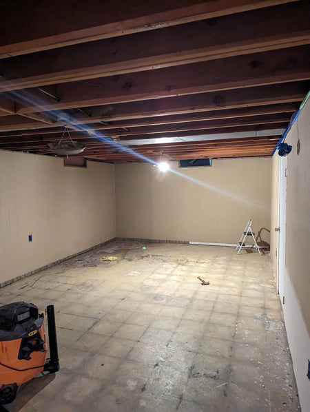 Image of a basement floor covered in mastic, showing the ghosting of tiles once under the carpet
