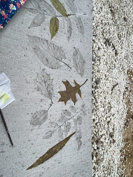 Close-up of concrete with leaf stencils, partially filled with natural green and brown shades, alongside acid staining tools