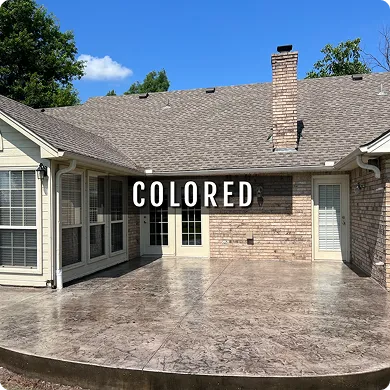 Brick house with a colored concrete patio under a clear blue sky.