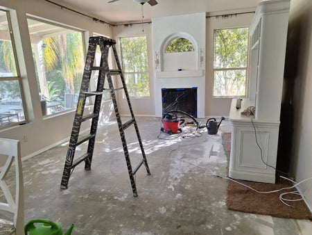 Living room with carpet removed, exposed concrete floor, prep tools, ladder, and fireplace before applying ColorWave Stone concrete stain