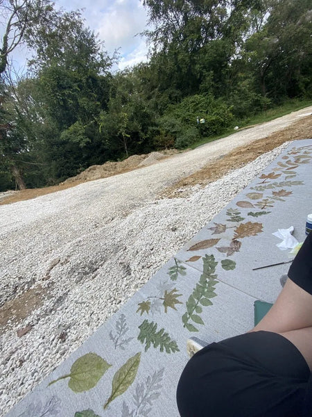Concrete walkway with multiple leaf stencils in green and brown tones created with EverStain acid stains, extending along a gravel driveway in a natural setting