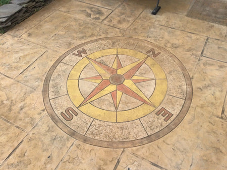 The faded stamped compass rose on the concrete driveway, barely visible due to weathering