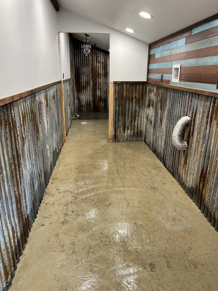 A multipurpose room with an uncolored concrete floor, surrounded by corrugated metal walls, before staining