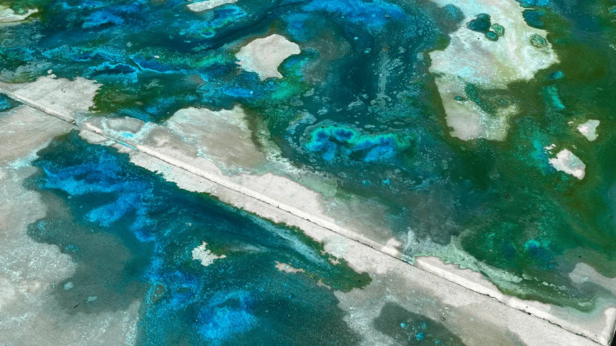 Close-up of a concrete surface with vibrant blue and green patterns created by the reaction of acid stain and Miracle Gro granules