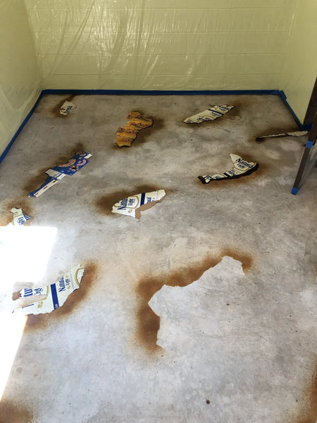 Torn cardboard pieces arranged on a concrete surface with acid stain applied 6-8 inches away, creating irregular veining patterns