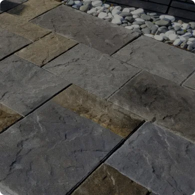 Patterned stone pavement with a mix of gray and brown stones, transitioning to pebbles.