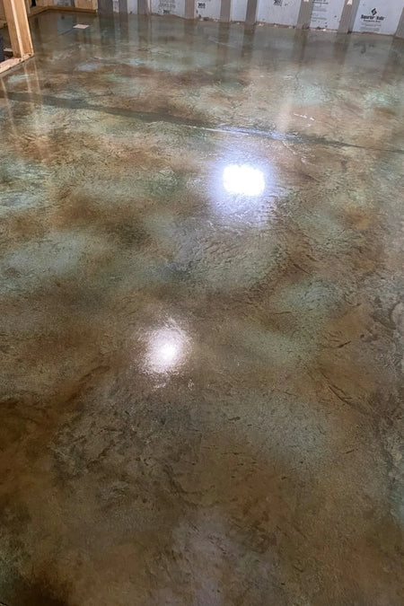 A photo of a concrete floor with the first coat of sealer applied, showing a glossy surface