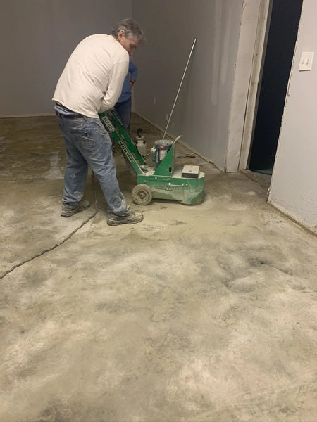 Man using a concrete grinder to remove stubborn carpet glue from a concrete floor