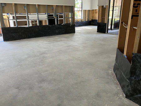 Image of a flood-damaged home interior with removed carpet and plank flooring, revealing a bare, untreated concrete floor