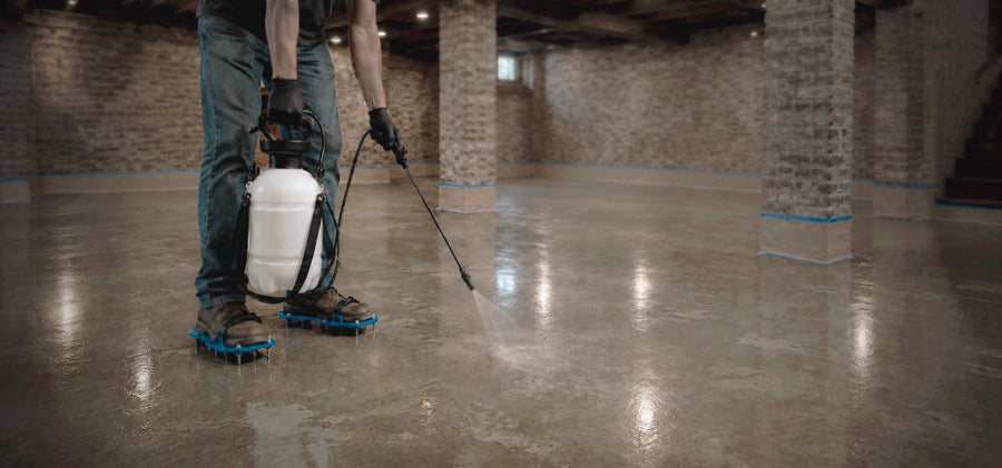 Contractor applying ProSeal Li penetrating water-based polymer concrete sealer with a pump sprayer, shallow depth of field showing the spray pattern on the slab