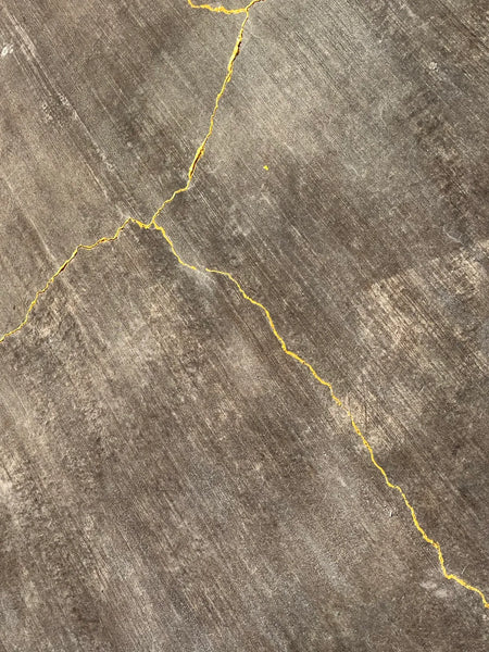 Close-up of a black-stained concrete patio featuring natural cracks highlighted with gold acrylic paint