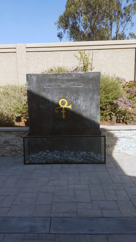 Before image showing a faded concrete monument dedicated to Prince, with his signature symbol engraved