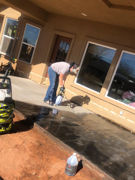DIY homeowner wearing spiked shoes and spraying Black Antiquing Stain onto a broom-finish concrete patio