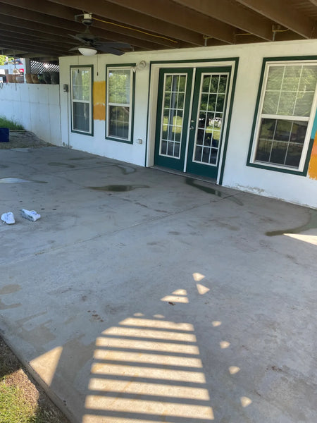 Broom-finish covered concrete patio stripped back to bare concrete, with traces of old paint still visible on the house wall, before acid staining