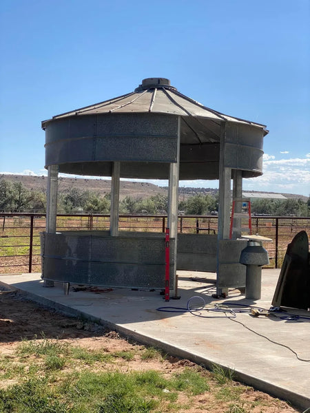 Freshly poured blank concrete patio slab beside a ranch house before turquoise acid staining, with a grain-bin bar under construction