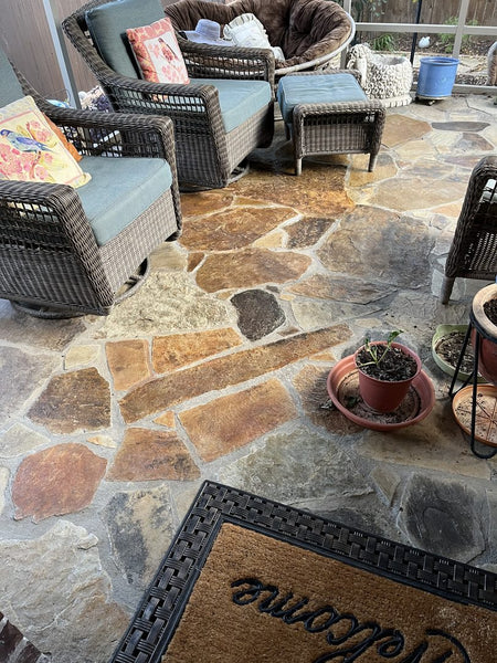 A flagstone patio featuring ColorWave stains in Rust, Amber, and Tangerine, with wicker furniture and potted plants enhancing the cozy outdoor space