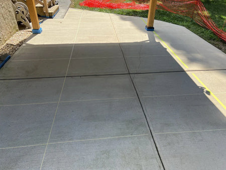 Covered scored concrete patio surface with tape creating a large tile design pattern, ready for staining