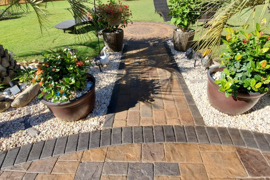 Wide view of a finished backyard patio with vibrant multi-tone pavers, tropical landscaping, and a fountain centerpiece