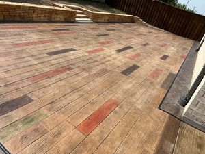 Wood-plank stamped concrete patio hand-stained plank by plank in Crimson, Cumin, Aztec Brown, and Tweed Antiquing with a charcoal border