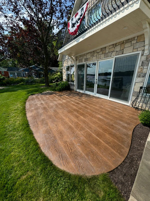 Curved lakefront wood-plank stamped concrete patio finished in warm Driftwood Antiquing stain with the grain and plank detail restored