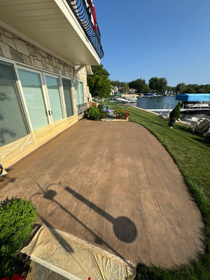 Wood-plank stamped concrete patio freshly stained with Driftwood Antiquing, wet and dark before drying and sealing, edges masked off
