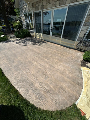 Sun-faded gray-tan wood-plank stamped concrete patio on a lakefront home before Driftwood Antiquing stain
