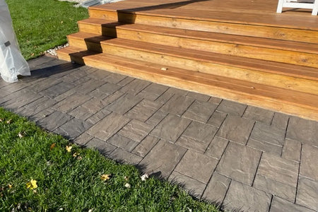 Finished dark charcoal stamped concrete pavers extending beside wooden deck steps and a green lawn