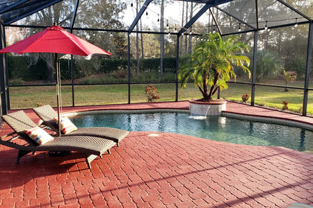 Finished Milano Red concrete pool deck with patio seating, lounge chairs, and red umbrella