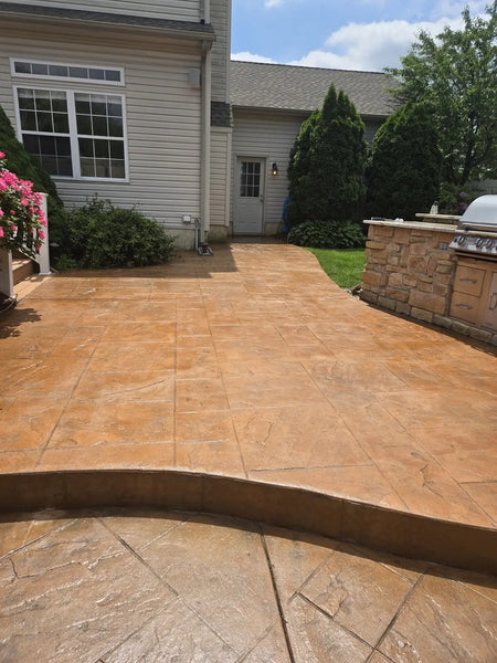 Raised stamped concrete patio beside a house and outdoor kitchen after warm Cumin EasyTint restoration