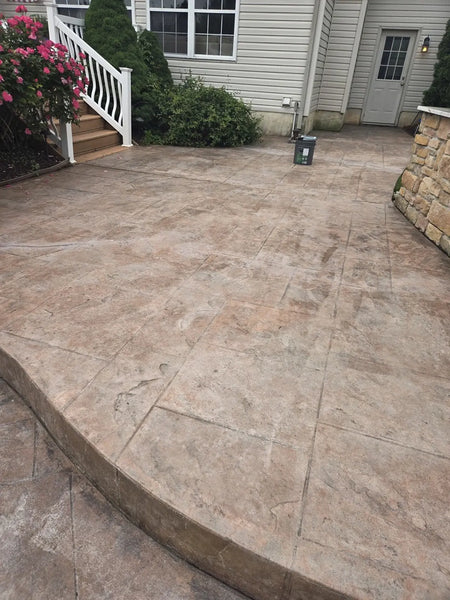 Faded stamped concrete patio beside a house with a bucket on the surface before Cumin EasyTint restoration