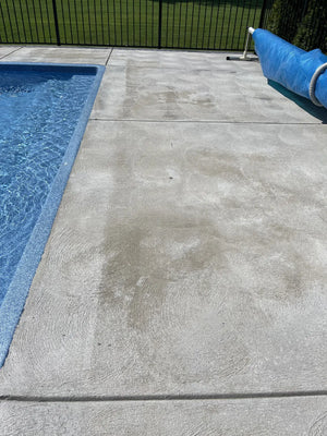 Blotchy swirl-finish concrete walkway beside a swimming pool and landscaped garden before Gray EasyTint restoration