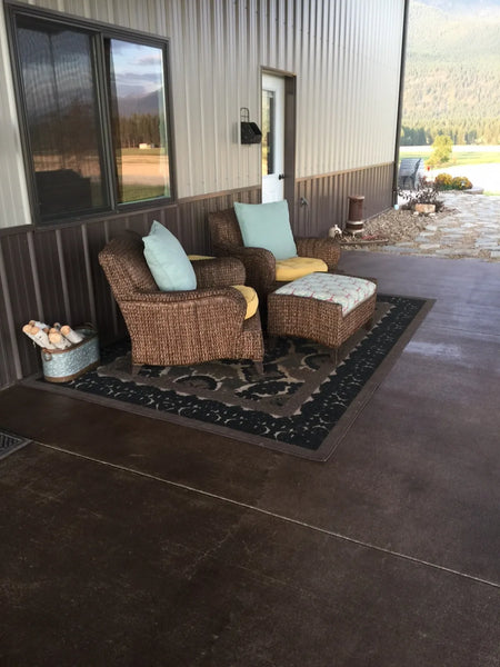 Covered pole barn concrete porch finished with variegated brown Driftwood Antiquing Stain and furnished with wicker seating