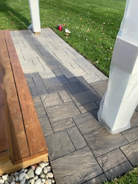 Stamped concrete pavers during Charcoal application, with darker treated sections around a protected porch post and lighter pavers ahead