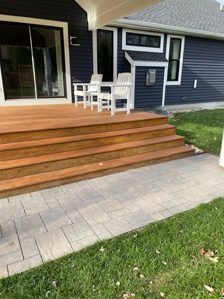 Back porch with wooden deck steps and a newly installed light gray stamped concrete paver area bordered by grass
