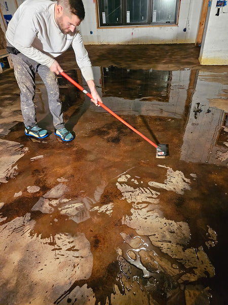 Second scrub-and-rinse pass removing loosened acid stain residue from a concrete floor with spiked shoes on until the water runs clear