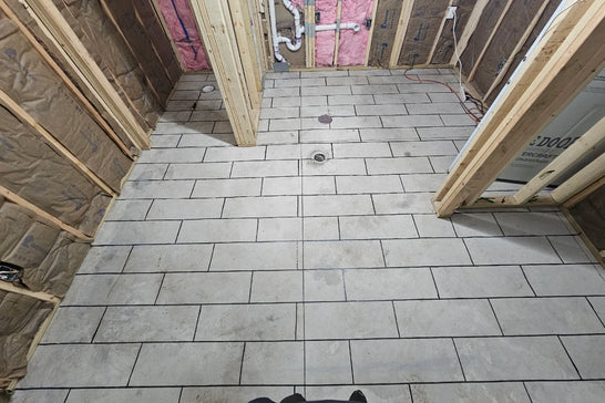 Masking tape laid out in a wood-plank pattern on a bare concrete bathroom floor before acid staining