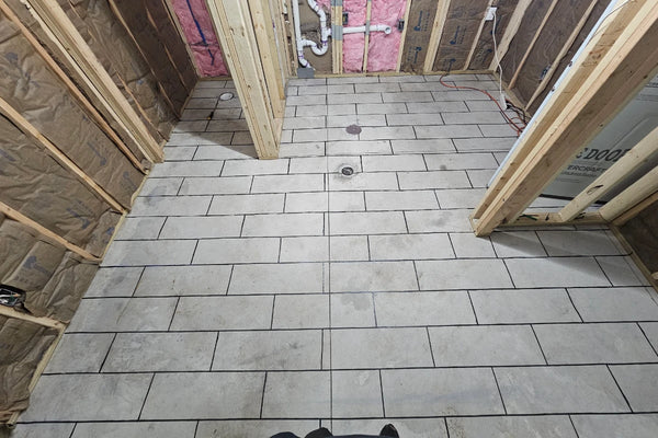 Masking tape laid out in a wood-plank pattern on a bare concrete bathroom floor before acid staining