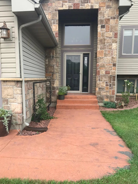 Residential stamped concrete walkway and front steps with a faded pinkish-orange surface leading to a stone-trimmed house